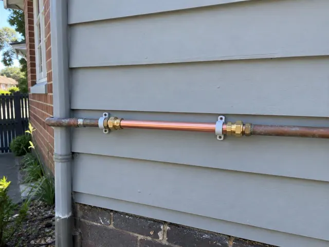 Repaired copper water pipe on an exterior weatherboard wall with brick corner in Rozelle