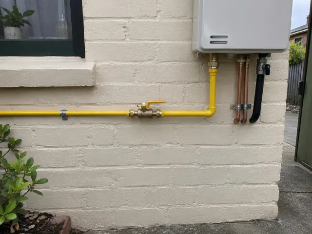 Exterior brick wall with yellow gas pipework, valves and meter beside a window in Annandale
