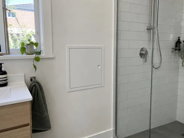 Small access panel in a bathroom wall beside a tiled shower and vanity in Lilyfield