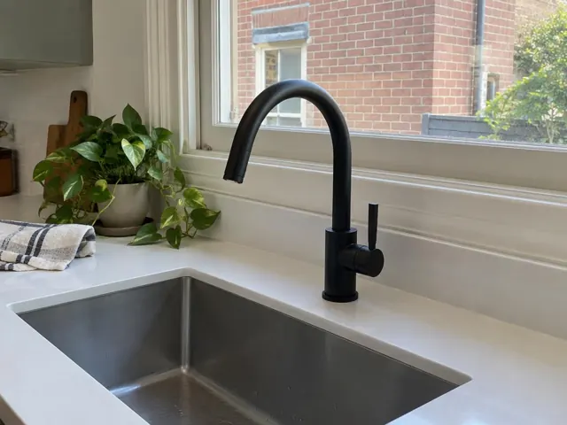Black gooseneck kitchen tap over stainless steel sink with white benchtop and window in Lilyfield